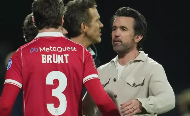 Actors and Wrexham owners Ryan Reynolds, center, and Rob McElhenney stand on the pitch after the fifth round FA Cup soccer match between Wrexham and Chelsea in Wrexham, Wales, Saturday, March 7, 2026. (AP Photo/Jon Super)