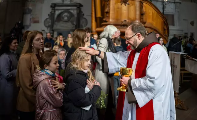 A priest distributes the Holy Communion during the Palm Sunday Mass at the St. Francis of Assisi Roman Catholic church in Vilnius, Lithuania, Sunday, March 29, 2026. (AP Photo/Mindaugas Kulbis)