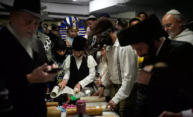 Jewish men and children, some dressed in costumes, read the Scroll of Esther as they celebrate the holiday of Purim in an underground parking garage as a precaution against possible Iranian missile attacks, in Tel Aviv, Israel, Monday, March 2, 2026. (AP Photo/Ohad Zwigenberg)