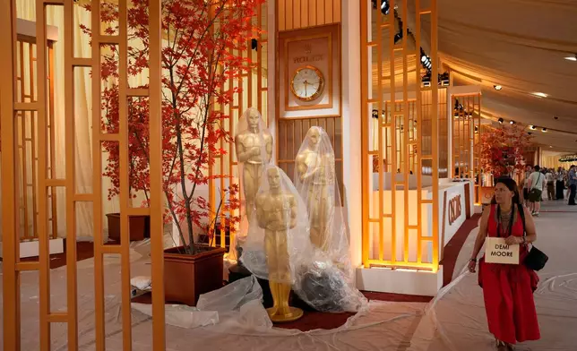 A person walks past Oscar statues wrapped in plastic in the red carpet area of the Dolby Theatre in Los Angeles, Friday, March 13, 2026, during preparations for Sunday's 98th Academy Awards ceremony. (AP Photo/John Locher)
