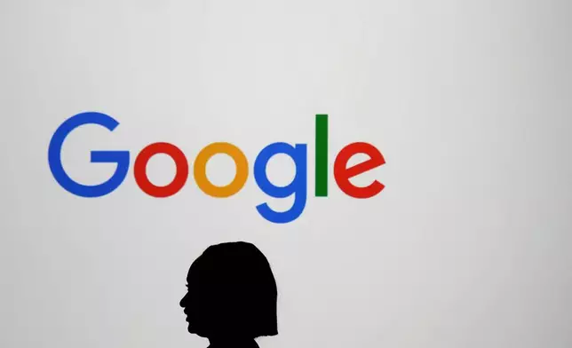 FILE - A woman walks by a giant screen with a logo at an event at the Paris Google Lab on the sidelines of the AI Action Summit in Paris, Feb. 9, 2025. (AP Photo/Thibault Camus, File)