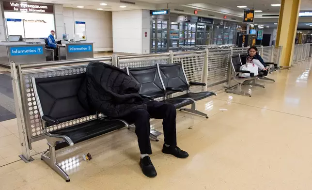 A man sleeps in the baggage claim area of Ronald Reagan National Airport, in Arlington, Va., Monday, March 16, 2026. (AP Photo/Cliff Owen)