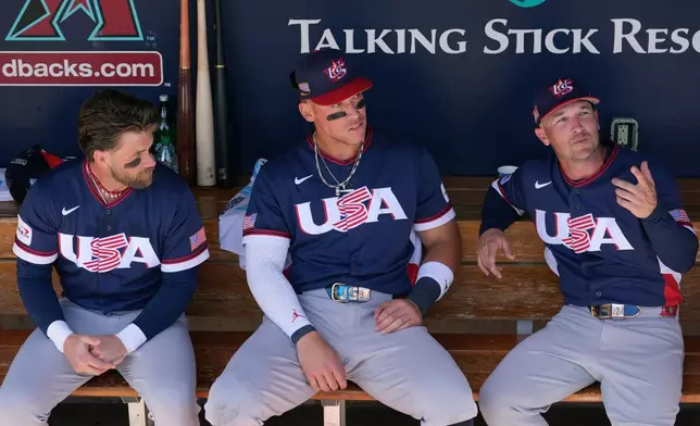Uniteds States' Bryce Harper, left, Aaron Judge, center, and Alex Bregman sit in the team dugout prior to an exhibition baseball game against the Colorado Rockies Wednesday, March 4, 2026, in Scottsdale, Ariz. (AP Photo/Ross D. Franklin)