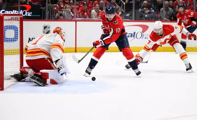 Washington Capitals center Dylan Strome (17) tries to get the puck past Calgary Flames goaltender Devin Cooley (1) and defenseman Kevin Bahl (7) during the first period of an NHL hockey game, Monday, March 9, 2026, in Washington. (AP Photo/Nick Wass)