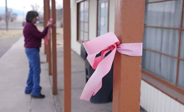 A woman hangs a pink ribbon on a pole Thursday, March 5, 2026, in Lyman, Utah, in honor of a woman that was killed a day earlier. (AP Photo/George Frey)