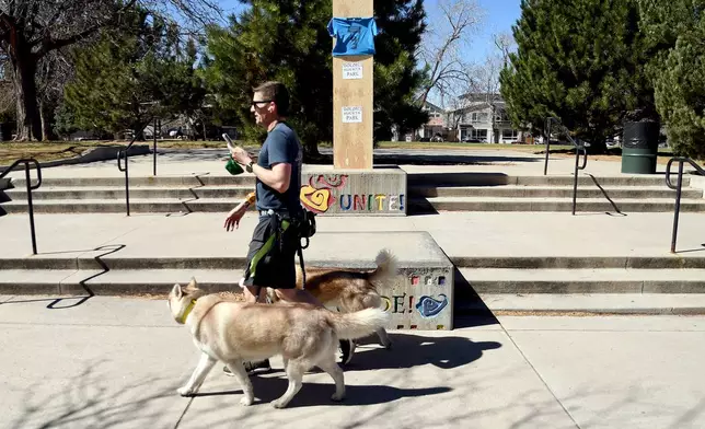 A man walks his dogs past a covered bust of César Chavez at César E. Chavez Park in Denver on Thursday, March 19, 2026. (AP Photo/Thomas Peipert)