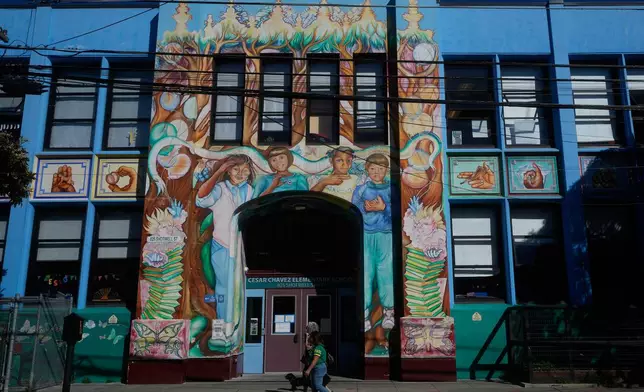 Pedestrians walk below a mural outside of César Chavez Elementary School in San Francisco, Wednesday, March 18, 2026. (AP Photo/Jeff Chiu)