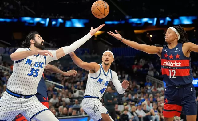 Orlando Magic center Goga Bitadze (35), guard Jalen Suggs (4) and Washington Wizards guard Tre Johnson (12) go after a rebound during the first half of an NBA basketball game, Tuesday, March 3, 2026, in Orlando, Fla. (AP Photo/John Raoux)