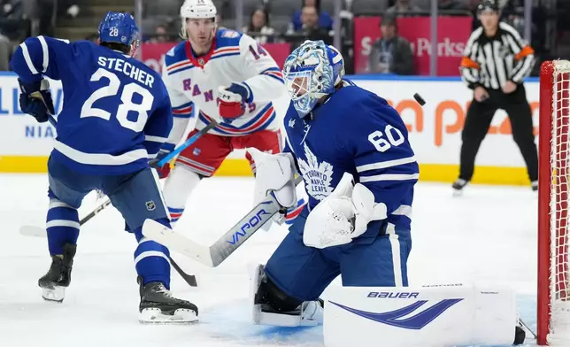 Toronto Maple Leafs goaltender Joseph Woll (60) makes a save as teammate Troy Stecher (28) and New York Rangers forward Taylor Raddysh (14) look on during the third period of an NHL hockey game in Toronto, Wednesday, March 25, 2026. (Nathan Denette/The Canadian Press via AP)