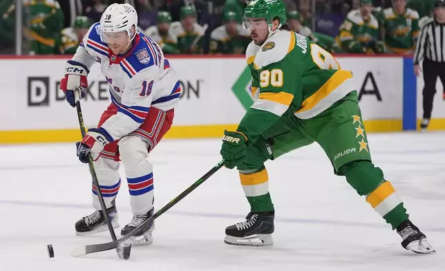 New York Rangers defenseman Urho Vaakanainen (18) and Minnesota Wild left wing Marcus Johansson (90) reach for the puck during the first period of an NHL hockey game, Saturday, March 14, 2026, in St. Paul, Minn. (AP Photo/Abbie Parr)