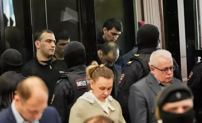 Men tried on the charges of involvement in a terror attack at the Crocus City Hall in March 2024, background, listen to the verdict from behind a glass cage at the Second Western District Military Court in Moscow, Russia, Thursday, March 12, 2026. (AP Photo/Pavel Bednyakov)