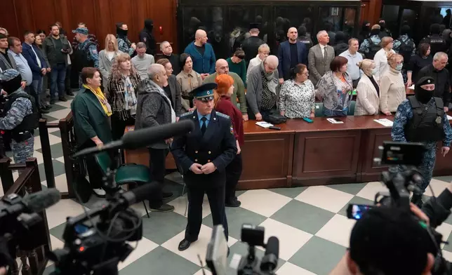 Men tried on the charges of involvement in a terror attack at the Crocus City Hall in March 2024, background, listen to the verdict from behind a glass cage as lawyers and journalists stand around at the Second Western District Military Court in Moscow, Russia, Thursday, March 12, 2026. (AP Photo/Pavel Bednyakov)