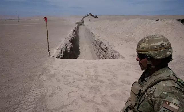 A soldier stands near a machine digging along the northern border at the Chacalluta border crossing, in Arica, Chile, Monday, March 16, 2026, as part of the measures to deter irregular migration. (AP Photo/Esteban Felix)