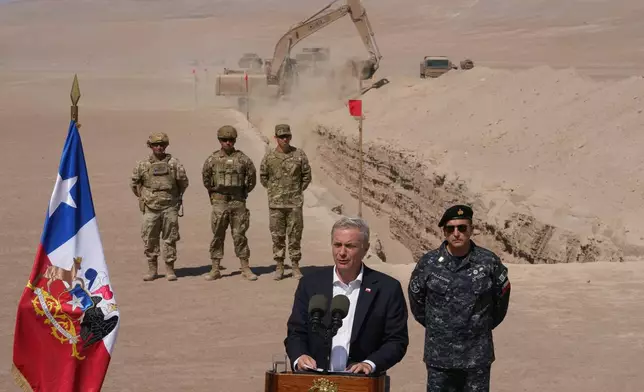 Chilean President Jose Antonio Kast gives a press conference as a machine digs, as part of measures to deter irregular migration, along the northern border at the Chacalluta border crossing, in Arica, Chile, Monday, March 16, 2026. (AP Photo/Esteban Felix)