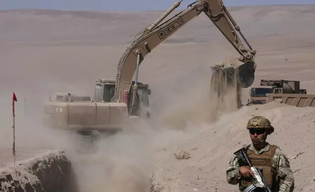 A soldier stands guard where a machine digs as part of measures to deter irregular migration along the northern border at the Chacalluta border crossing, in Arica, Chile, Monday, March 16, 2026. (AP Photo/Esteban Felix)