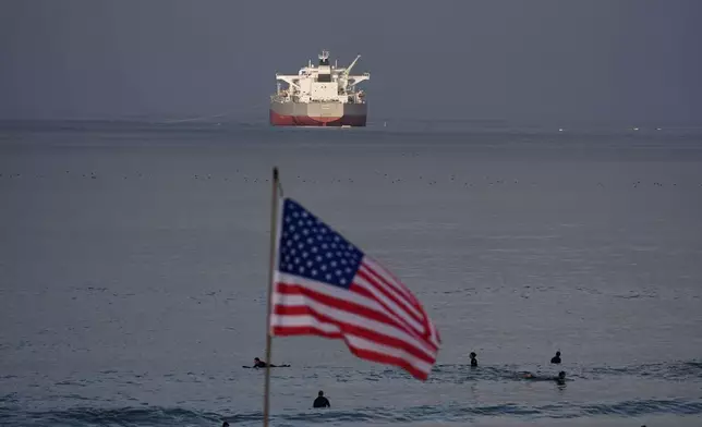 Surfers wait for waves on El Porto Beach as the crude oil tanker "Chios" has its cargo pumped into the Chevron Products Company refinery, one of California's largest petroleum processing facilities, in El Segundo, Calif., on Wednesday, March 4, 2026. (AP Photo/Damian Dovarganes)