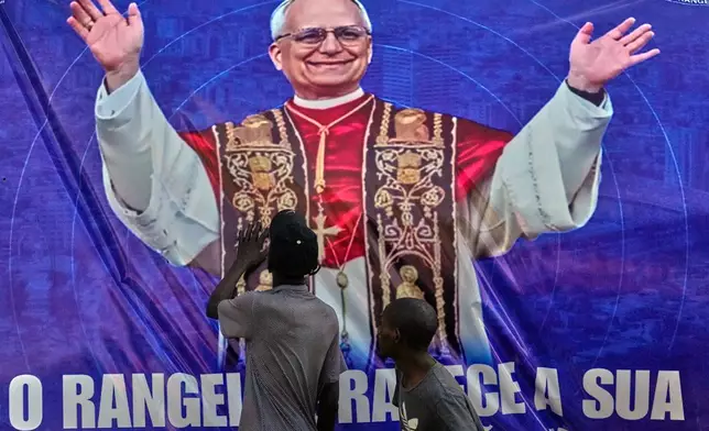People touch a banner bearing an image of Pope Leo XIV in Luanda, Angola, Monday, April 20, 2026. (AP Photo/Themba Hadebe)