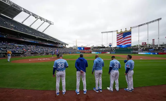 Coaches for the Kansas City Royals stand for the national anthem at Kauffman Stadium before a baseball game against the Baltimore Orioles, Wednesday, April 22, 2026, in Kansas City, Mo. (AP Photo/Charlie Riedel)