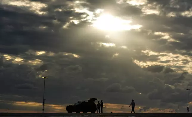 People gather under storm clouds in a parking lot outside Kauffman Stadium after a baseball game between the Kansas City Royals and the Chicago White Sox, Saturday, April 11, 2026, in Kansas City, Mo. (AP Photo/Charlie Riedel)