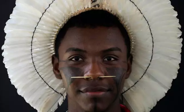 An Indigenous man wearing traditional face paint, feather headdress and piercing poses for a portrait during the opening of the "Acampamento Terra Livre," or Free Land Encampment, Brazil's largest annual Indigenous mobilization that focuses on land rights and environmental protection, in Brasilia, Brazil, Monday, April 6, 2026. (AP Photo/Eraldo Peres)