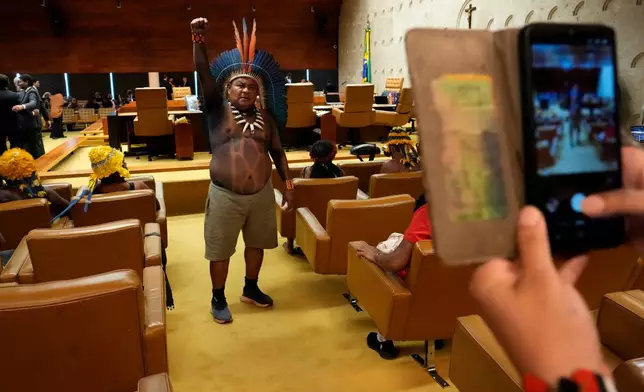 Tupinamba Indigenous leader Gilson Tupinamba raises a fist while posing for a photo inside Brazil's Supreme Court courtroom before a session, where justices will discuss a case about reducing the size of Jamanxim National Park, in Brasilia, Wednesday, April 8, 2026. (AP Photo/Eraldo Peres)