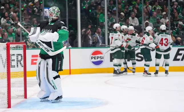 Minnesota Wild players, right, celebrate a goal by Ryan Hartman as Dallas Stars goaltender Jake Oettinger, left, stands in his crease during the second period in Game 1 of a first-round NHL Stanley Cup playoffs hockey series, Saturday, April 18, 2026, in Dallas, Texas. (AP Photo/Julio Cortez)