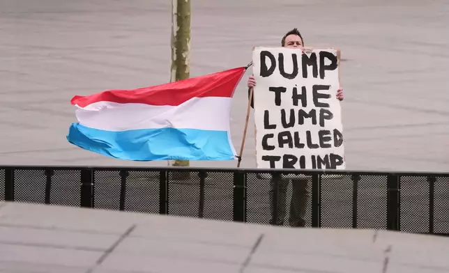 A man holds the flag of Luxembourg and a placard as he demonstrates outside a meeting of EU foreign ministers at the European Council building in Luxembourg, Tuesday, April 21, 2026. (AP Photo/Virginia Mayo)
