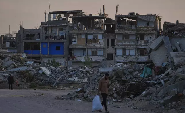 FILE - Palestinians walk along a street surrounded by buildings destroyed during Israeli air and ground operations in Khan Younis, southern Gaza Strip, on April 9, 2026. (AP Photo/Abdel Kareem Hana, File)