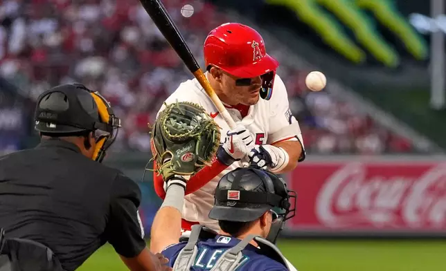 Los Angeles Angels' Mike Trout, center, is hit by a pitch as Seattle Mariners catcher Cal Raleigh, right, and home plate umpire Ramon De Jesus watch during the first inning of an opening-day baseball game Friday, April 3, 2026, in Anaheim, Calif. (AP Photo/Mark J. Terrill)