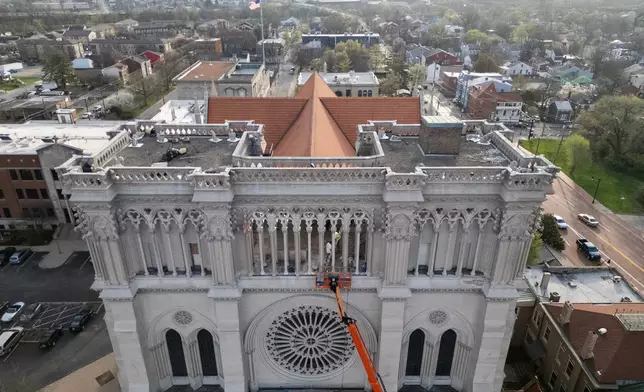 Workers are seen beyond an orange cherry picker high on the Cathedral Basilica of the Assumption, known as "America's Notre Dame," as the final new terra cotta gargoyle is secured with straps to the left, in Covington, Ky., on Tuesday, March 31, 2026. (AP Photo/Carolyn Kaster)