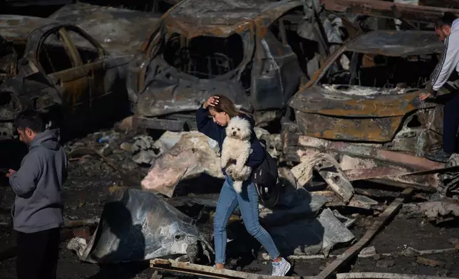 FILE - A woman holds her dog as she walks past burned cars a day after an Israeli airstrike in Beirut, Lebanon, Thursday, April 9, 2026. (AP Photo/Emilio Morenatti, File)