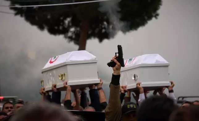 FILE - A gunman fires his gun as men carry the coffins with the bodies of Pierre Mouawad, an official with the anti-Hezbollah Lebanese Forces party, and his wife during their funeral in Yahshush, in Lebanon, Tuesday, April 7, 2026. (AP Photo/Emilio Morenatti, File)