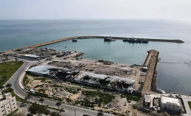 Backdropped by ships in the Strait of Hormuz, damage, according to local witnesses caused by several recent airstrikes during the U.S.-Israel military campaign, is seen on a fishing pier in the port of Qeshm island, Iran, Monday, April 13, 2026. (AP Photo/Asghar Besharati)