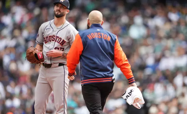 A trainer comes to the mound to talk with Houston Astros starting pitcher Cody Bolton during the second inning of a baseball game against the Seattle Mariners, Sunday, April 12, 2026, in Seattle. (AP Photo/Lindsey Wasson)