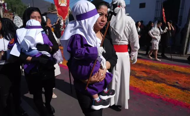 Women carry children dressed as penitents knows as "cucuruchos" on the sidelines of La Merced church's Good Friday procession during Holy Week in Antigua, Guatemala, Friday, April 3, 2026. (AP Photo/Moises Castillo)