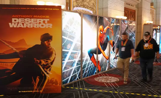 CinemaCon attendees walk past advertisements for upcoming films including "Desert Warrior" and "Spiderman: Brand New Day" during the opening day of CinemaCon 2026, the official convention of Cinema United, on Monday, April 13, 2026, at Caesars Palace in Las Vegas. (AP Photo/Chris Pizzello)