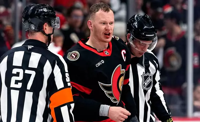 Ottawa Senators winger Brady Tkachuk's lip bleeds as he is escorted by officials after fighting with Carolina Hurricanes' K'andre Miller during the second period in Game 4 of a first-round NHL Stanley Cup playoff hockey series, Saturday, April 25, 2026, in Ottawa, Ontario. (Justin Tang/The Canadian Press via AP)