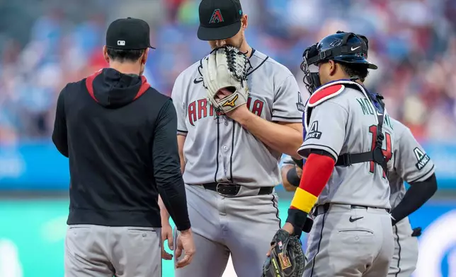Arizona Diamondbacks starting pitcher Mike Soroka, center, looks down as pitching coach Brian Kaplan, left, and catcher Gabriel Moreno, right, come out to talk to him after the three-run home run by Philadelphia Phillies' Brandon Marsh during the first inning of a baseball game, Friday, April 10, 2026, in Philadelphia. (AP Photo/Chris Szagola)