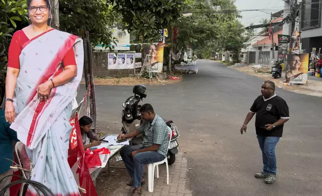 A voter, right, arrives to check his name at an assistance booth set up by party workers as a candidate's cut out photo is displayed on left during the Kerala state election in Kochi, India, Thursday, April 9, 2026. (AP Photo/ R S Iyer)