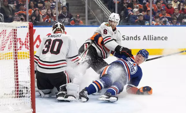 Chicago Blackhawks goalie Spencer Knight (30) makes the save as Sam Rinzel (6) and Edmonton Oilers' Trent Frederic (10) crash the net during the second period of an NHL game, in Edmonton on Thursday April 2, 2026. (Jason Franson/The Canadian Press via AP)