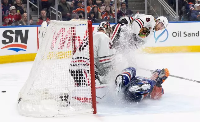 Chicago Blackhawks goalie Spencer Knight (30) makes the save as Sam Rinzel (6) and Edmonton Oilers' Trent Frederic (10) crash the net during the second period of an NHL game, in Edmonton on Thursday April 2, 2026. (Jason Franson/The Canadian Press via AP)