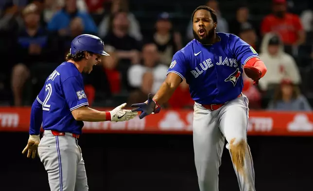 Toronto Blue Jays' Vladimir Guerrero Jr. (27) is greeted by Toronto Blue Jays' Ernie Clement (22) after scoring on a sacrifice fly from Toronto Blue Jays designated hitter Eloy Jimenez (74) during the eighth inning of a baseball game Tuesday, April 21, 2026, in Anaheim, Calif. (AP Photo/Caroline Brehman)
