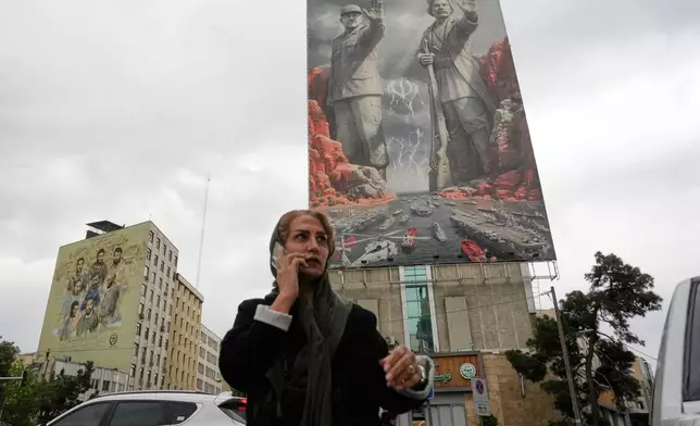 A woman talks on her cellphone as she walks past a billboard showing Rais Ali Delvari, a national hero in an early 1900 uprising against British forces in southern Iran in the Persian Gulf, right, and the late Revolutionary Guard's navy chief Alireza Tangsiri, who was killed in the U.S.-Israeli strike in late March 2026, commanding the closure of the Strait of Hormuz, on a building at a square in downtown Tehran, Iran, Monday, April 20, 2026. (AP Photo/Vahid Salemi)