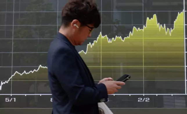 A person walks in front of an electronic stock board chart showing Japan's Nikkei index at a securities firm, Tuesday, April 28, 2026, in Tokyo. (AP Photo/Eugene Hoshiko)