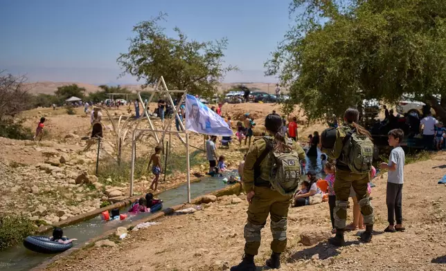 Israeli soldiers look on as Israeli settlers and others enjoy a day at a spring in the Jordan Valley during Israel's Independence Day, in Auja, in the occupied West Bank, Wednesday, April 22, 2026.(AP Photo/Ohad Zwigenberg)