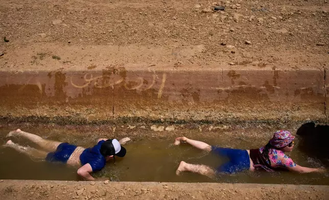 Two boys slide down into a spring as Israeli settlers and others enjoy a day in the Jordan Valley during Israel's Independence Day, in Auja, in the occupied West Bank, Wednesday, April 22, 2026.(AP Photo/Ohad Zwigenberg)