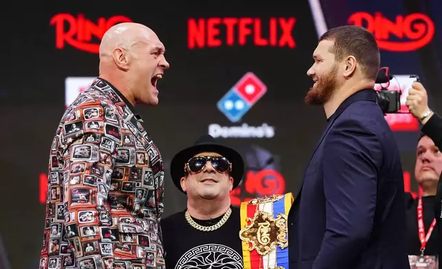 Boxwers Tyson Fury, left and Arslanbek Makhmudov face off as Ring Magazine CEO Rick Reeno, looks on during a press conference, Thursday April 9, 2026, in London. (Bradley Collyer/PA via AP)