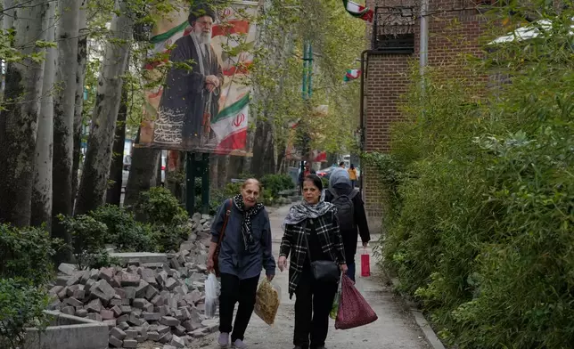 Women walk past a banner depicting the late Iranian Supreme Leader Ayatollah Ali Khamenei, who was killed in the U.S. and Israel strikes on Feb. 28, in northern Tehran, Iran, Sunday, April 12, 2026. (AP Photo/Vahid Salemi)