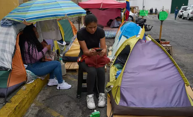 Sandra Rosales uses her phone while camping outside the gates of a Bolivarian National Police detention center where her husband, Dionnys Quintero, is being held on political grounds in Caracas, Venezuela, Thursday, March 12, 2026. (AP Photo/Ariana Cubillos)