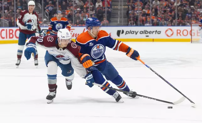 Colorado Avalanche's Sam Malinski (70) and Edmonton Oilers' Jack Roslovic (28) battle for the puck during overtime NHL action, in Edmonton, Alberta, on Monday, April 13, 2026. (Jason Franson/The Canadian Press via AP)